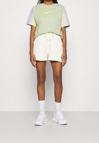 Světle zelené oversize tričko Nike s fialovými a krémovými rukávy, doplněné krémovými šortkami s kapsami a bílými teniskami.