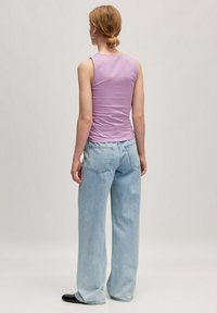 Lila mouwloze top met een aansluitend ontwerp, gecombineerd met lichtblauwe wijde jeans. Gladde texturen en minimale stiksels zijn zichtbaar.