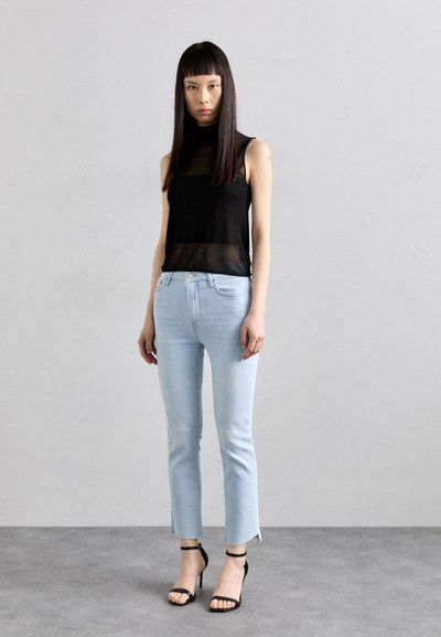 Svart gjennomsiktig ermløs topp sammen med lyseblå, cropped jeans med splitt i kanten. Modellen har på seg svarte høye sandaler med stropper.
