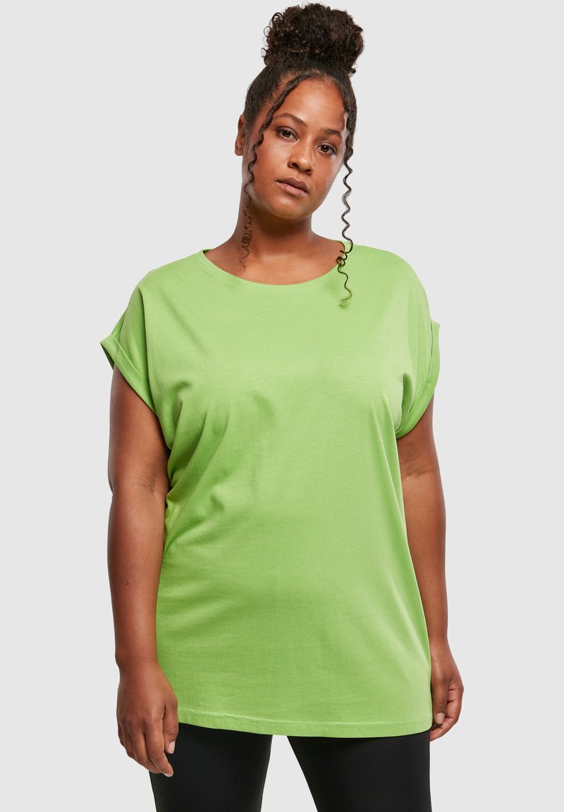 Tricou verde lime, lejer, cu mâneci îndoite, guler rotund și textură netedă. Purtați cu colanți negri, vedere din față.