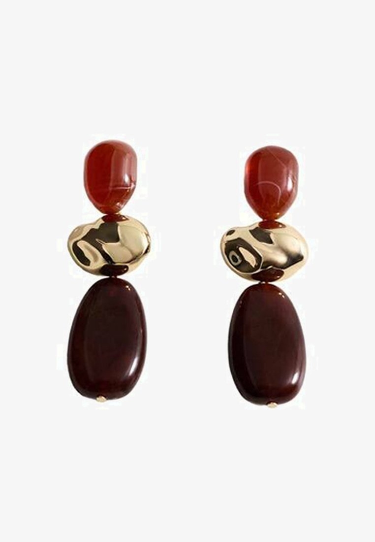 Des boucles d'oreilles rouges et dorées avec deux pierres rouges arrondies, un accent doré au motif ondulé, et deux pierres ovales rouge foncé en dessous.