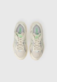 Baskets de sport beige clair avec des panneaux en mesh, des accents argentés et un logo vert. Présentent un bout arrondi et des lacets plats pour un ajustement sûr.