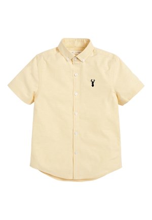 Chemise à manches courtes, jaune pâle, à boutons avec col, arborant un petit logo tête de cerf noir sur le côté gauche de la poitrine.