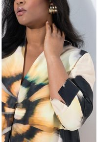 Bunt gemusterte Bluse mit floralem Muster, aus leichtem Stoff gefertigt. Das Design umfasst einen V-Ausschnitt und schwarze Akzente an den Ärmeln.