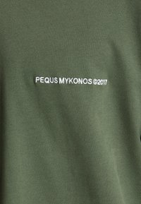 T-shirt en coton vert avec le texte brodé blanc "PEQUS MYKONOS ©2017" à l'avant, présentant une texture lisse et unie.