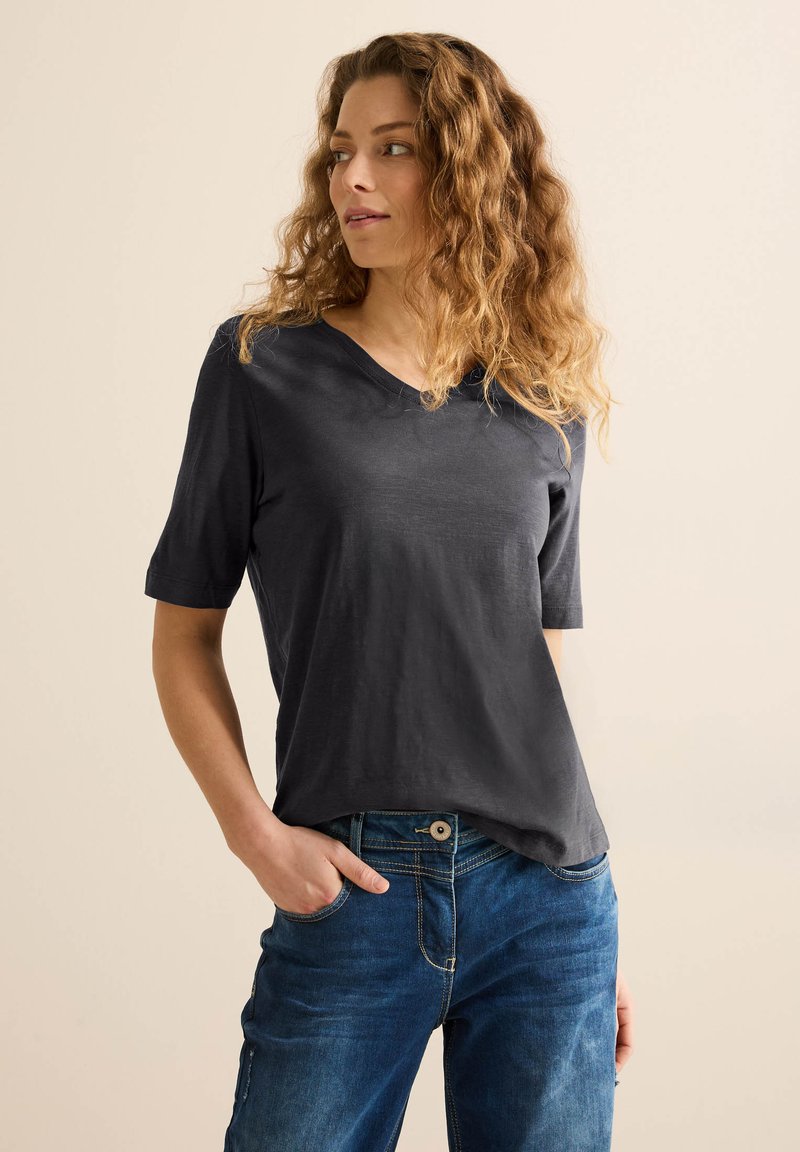 Camiseta de cuello en V de manga corta en gris oscuro, fabricada con un tejido suave, exhibida con jeans de mezclilla azules, destacando un ajuste relajado y un estilo casual.