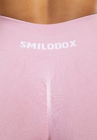 Roze leggings met een ribbelstructuur. Heeft een brede tailleband met de tekst "SMILODOX" in het wit. Geen extra patronen of accenten.