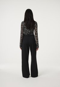 Zwarte high-waisted broeken met wijde benen, gecombineerd met een aansluitend, doorschijnend long-sleeve top met een handgeschreven patroon in het wit.