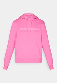 Rosa hettegenser laget av en bomullsblanding, med en frontlomme og "BJÖRN BORG"-logo i hvitt. Glatt tekstur, uformelt design.