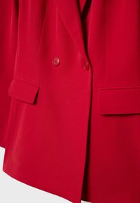 Rdeč blazer iz gladkega blaga, z dvorednim zapenjanjem, dvema gumboma in žepki z zanko ter ostrim ovratnikom.