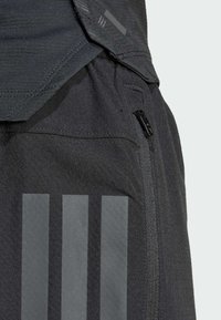 Shorts atléticos oscuros confeccionados con tela texturizada, que cuentan con un bolsillo con cremallera y tres acentos de rayas verticales en un tono más claro.