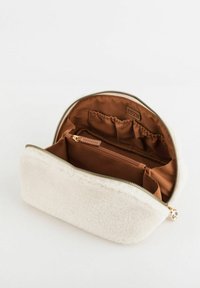 Biała kosmetyczka z polaru z brązową tkaninową wyściółką, zamkiem błyskawicznym i licznymi kieszeniami do zorganizowanego przechowywania. Złote akcenty metalowe.