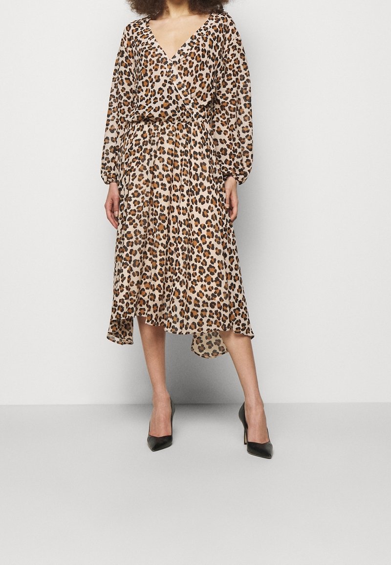 Robe en tissu léger avec imprimé léopard, dotée d'un décolleté en V, de longues manches bouffantes et d'un ourlet asymétrique fluide. Des talons noirs viennent compléter le look.