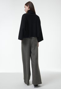 Schwarzer, verkürzter Rollkragenpullover kombiniert mit hochtaillierten, weit geschnittenen grauen Hosen mit strukturiertem Muster. Glattes Material und taillierte Passform.