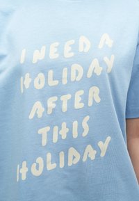 Ανοιχτό γαλάζιο βαμβακερό t-shirt με έντονο λευκό κείμενο που λέει «ΧΡΕΙΑΖΟΜΑΙ ΔΙΑΚΟΠΕΣ ΜΕΤΑ ΑΠΟ ΑΥΤΕΣ ΤΙΣ ΔΙΑΚΟΠΕΣ», με άνετο λαιμόκοψη τύπου crew.