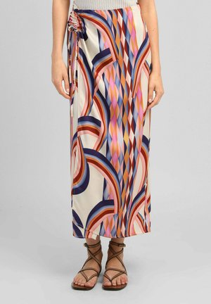 Jupe à motifs géométriques colorés avec un détail froncé sur le côté, portée avec des sandales marron à brides et un top beige sans manches.