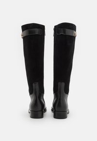 Bocanci negri din suede, până la genunchi, cu accente din piele, având detalii din metal cu finisaj auriu, textură și un design cu toc subțire.