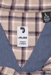 Geverfd beige en bruine stof met een effen blauwe rand. Een label geeft "J&JOY" aan, met maat L en herkomst uit België. Gevoeld patroon detail zichtbaar.