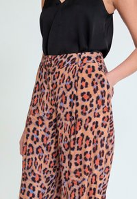 Pantalones con estampado de leopardo en tela suave; cuentan con piernas anchas, una cintura alta, bolsillos laterales y una mezcla de colores marrón, negro y naranja.