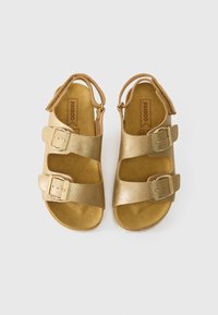 Kuldsetel sandaalidel on kaks laia rihma, millel on metallist pandlad. Ülemine materjal on sile ja läikiv. Pehme nahast siseosa.