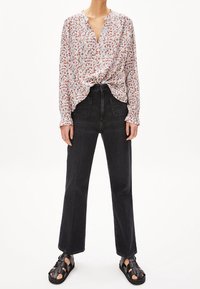 Kvinna klädd i en vit blommig långärmad blus instoppad i svarta högmidjade raka jeans och svarta sandaler med öppen tå.