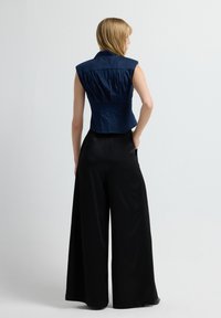 Top sin mangas de color azul marino con un collar estructurado y espalda plisada, combinado con pantalones de pierna ancha negros. Tejido suave con un corte a medida.