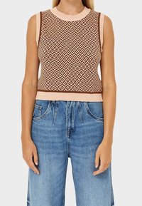Gestricktes ärmelloses Oberteil in Braun und Pink mit geometrischem Muster, ausgestattet mit einem gerippten Rundhalsausschnitt und passendem Taillenbund, kombiniert mit blauen Jeans.