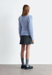 Helles blauer, flauschiger Pullover mit Puffärmeln, kombiniert mit einem dunklen, plissierten Rock, grauen Rippensocken und schwarzen Schuhen.