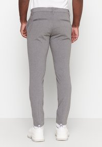Gray tailored trousers with a slim fit, made of textured fabric, featuring back pockets and side seams. Worn with white sneakers.
