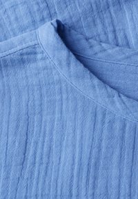 Tessuto di cotone azzurro chiaro con una superficie morbida e testurizzata e un collo rotondo, caratterizzato da sottili linee verticali e dettagli di cucitura visibili.