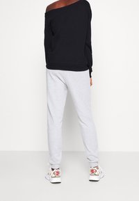 Sudadera negra sin hombros, pantalones de chándal grises y zapatillas con un diseño blanco y acentos coloridos. Ajuste casual, textura suave.