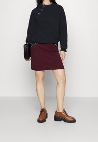 Černá mikina s volánovým límcem a třemi knoflíky, doplněná vínovou sukní s cvočky a hnědými šněrovacími botami.