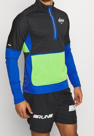 Mężczyzna w czarnej, niebieskiej i zielonej sportowej bluzie z zamkiem i czarnych szortach z białym tekstem "RUN".