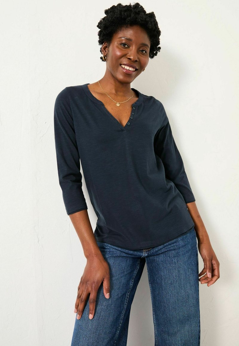 Navy blue, long-sleeve henley shirt with a V-neck and button accents; soft fabric with a relaxed fit paired with high-waisted jeans.