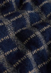 Tmavomodrá károvaná deka s jemnou textúrou a striedavými tkanými vzormi v modrej a béžovej farbe. Materiál pôsobí útulne a teplo.