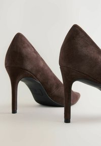 Korkeat ruskeat nahan mokka-kengät, joissa on terävä kärki ja kapea stiletto-korko. Tekstuuriltaan ne ovat pehmeät, ja muotoilussa on saumaton yläosa ja kaareva siluetti.