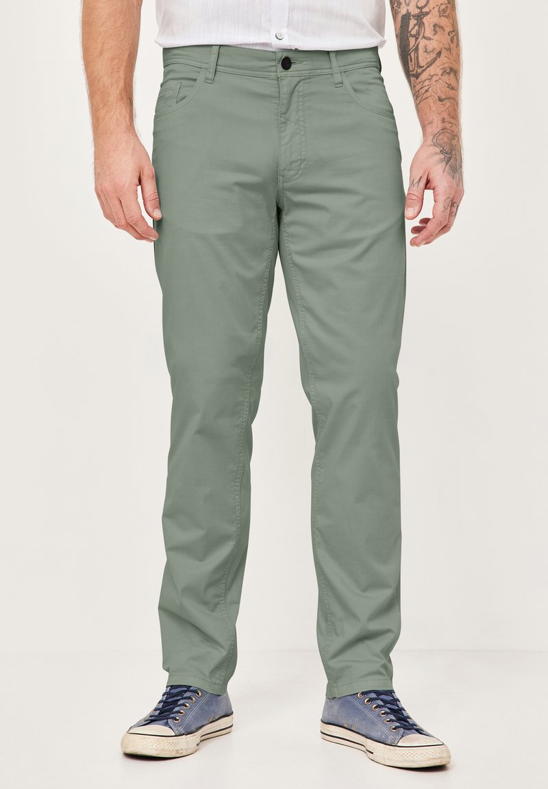 Grüne Baumwollchinos mit schlanker Passform, ausgestattet mit einem Knopfverschluss, Vordertaschen und einer glatten Textur, kombiniert mit blauen lässigen Sneakern.