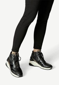 Schwarze High-Top-Sneaker mit beigen Leopardenprint-Akzenten, Schnürung vorne, seitlichem Reißverschluss und einer Keilsohle für zusätzlichen Halt und Höhe.