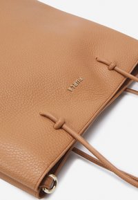 Borsa a spalla in pelle marrone con texture, logo dorato e chiusura a coulisse. Include un dettaglio con anello in metallo dorato sul lato.