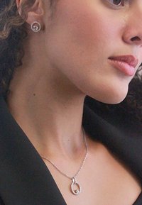 Collana d'argento con un pendente ovale e abbellimenti in pietre preziose, abbinata a orecchini a cerchio abbinati. Entrambi mostrano dettagli intricati.