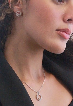 Zilveren ketting met een ovale hanger en edelsteenversieringen, gecombineerd met bijpassende ronde studoorbellen. Beide tonen ingewikkelde details.