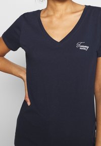 Marinblå bomulls-T-shirt med V-ringning och korta ärmar, med en liten vit broderad "Tommy Jeans"-logotyp på bröstet.