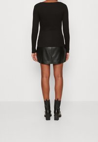 Schwarzes, geripptes Langarmoberteil kombiniert mit einem schwarzen Minirock aus Kunstleder und knöchelhohen Stiefeletten mit Blockabsatz, Ansicht von hinten.