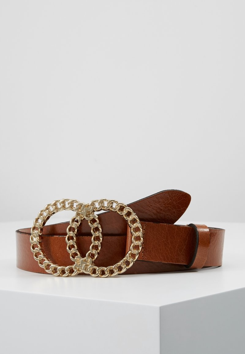 Ceinture en cuir marron avec une grande boucle dorée à double maillon reposant sur une surface blanche sur un fond uni.