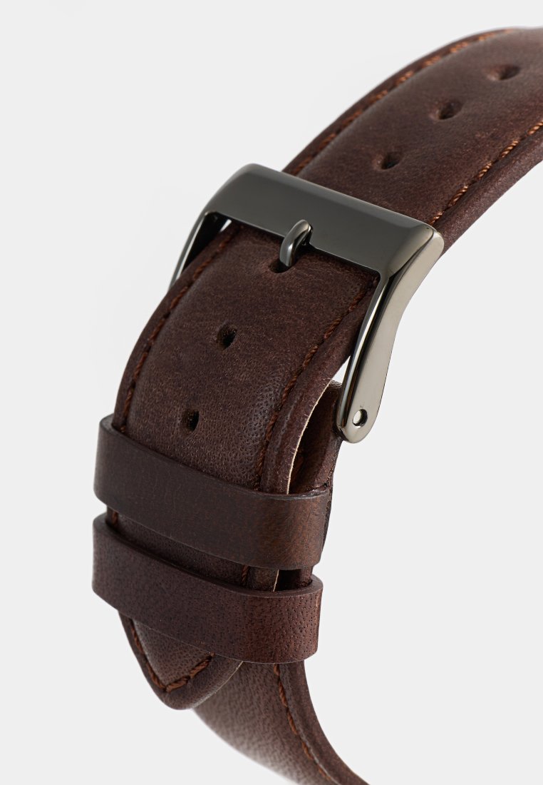 Correa de reloj de cuero marrón con acabado texturizado, que presenta una hebilla de metal plateado, orificios laterales para ajuste y un doble lazo de seguridad.