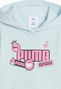 En ljusblå hoodie med en stor rosa grafik med texten "PUMA" och "HELLO KITTY OCH VÄNNER", prydd med karaktärsillustrationer och hjärtan.