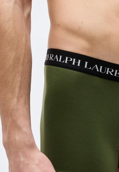 Αρσενικός κορμός και χέρι που φορούν εσώρουχα ελιάς με μαύρη μέση που δείχνει το όνομα της μάρκας "Polo Ralph Lauren".