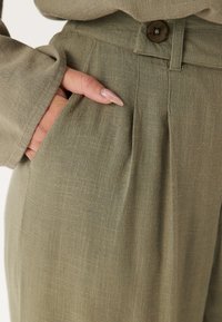 Olivgröna linnejoggers med en framficka, veckad design och en knappknäppning. Strukturerad tyg med en avslappnad passform.