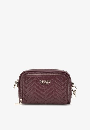Donkerpaarse doorgestikte crossbodytas met voorvak met ritssluiting en zilveren Guess-logo en ritssluitingaccenten, met sleutelring aan de zijkant.