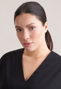 Czarny top z dekoltem w serek wykonany z gładkiej tkaniny, z krótkimi rękawami i luźnym krojem, na modelce z prostymi włosami na neutralnym tle.